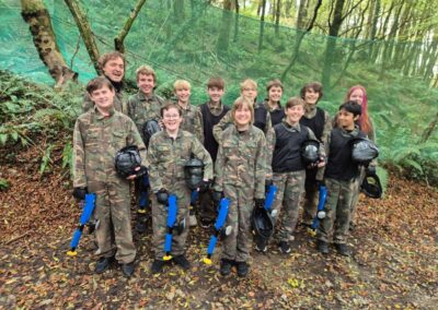 Teenagers in camouflage gear with paintball guns in a wooded area.