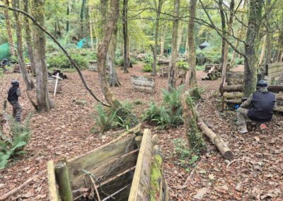 Paintball players in a wooded course, taking cover behind wooden bunkers and trees.