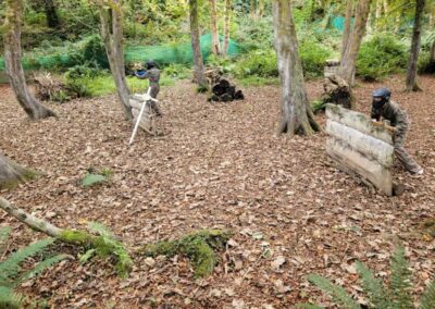 Two players in camouflage gear playing paintball in a forest setting.