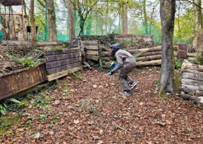 Person playing paintball in outdoor arena, wearing camouflage and safety gear.