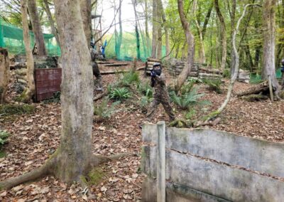 Players in camouflage gear playing paintball in a wooded area, using bunkers for cover.
