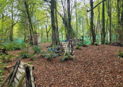 Paintball players taking cover in a wooded area with foliage and bunkers.