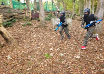 Two players in camouflage gear running during a paintball game in the woods.