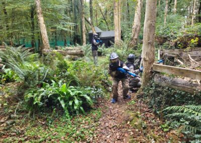 Paintball players in camouflage gear aiming guns in a wooded area.